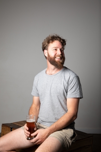 Young man sitting, holding a glass of beer, relaxed and happy