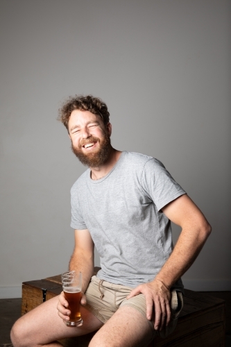 Young man sitting, holding a glass of beer, relaxed and happy