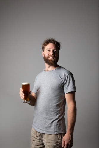 Man sitting, holding a glass of beer, relaxed and happy - Australian Stock Image