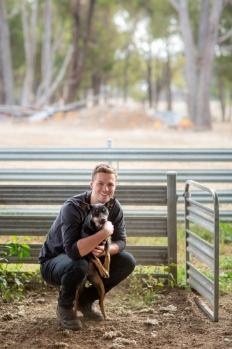 Young man squatting down with kelpie dog - Australian Stock Image