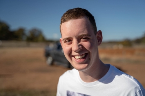 Young man standing outdoors under the sun smiling - Australian Stock Image