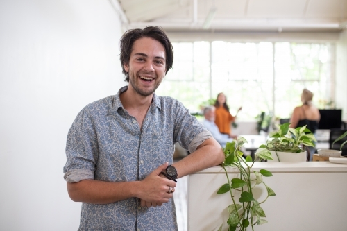 Young man standing, smiling in white office - Australian Stock Image