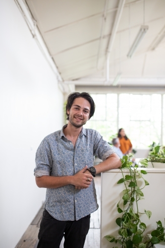 Young man standing, smiling in white office - Australian Stock Image