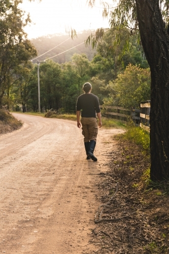 Young man walking down winding dirt road on bush walk at sunset outside rural property