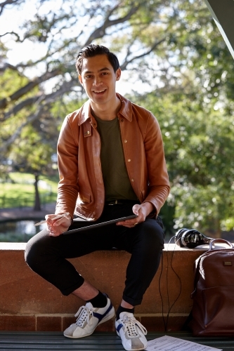 Young man with dark hair outside holding device with headphones at park - Australian Stock Image