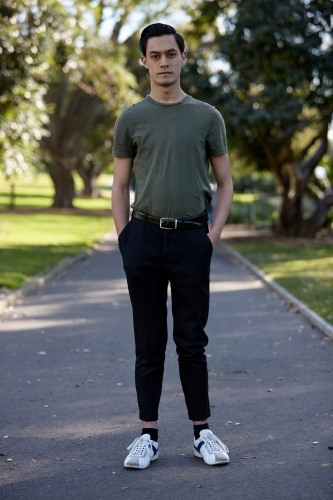 Young man with dark hair standing outside at park - Australian Stock Image