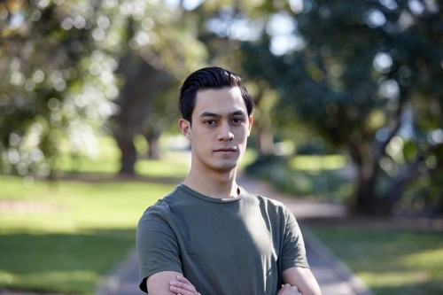 Young man with dark hair standing outside at park - Australian Stock Image