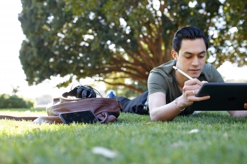 Young man with dark hair writing on his device at park