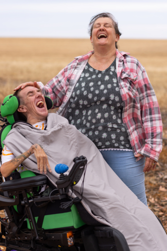 Young man with disability laughing with mother standing on dirt road in country - Australian Stock Image