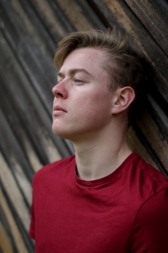 Young melancholy caucasian man modelling in front of a wooden panelled background - Australian Stock Image