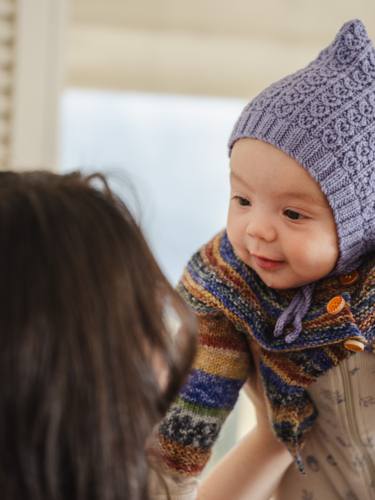 Young mother holding baby wearing beanie inside home - Australian Stock Image