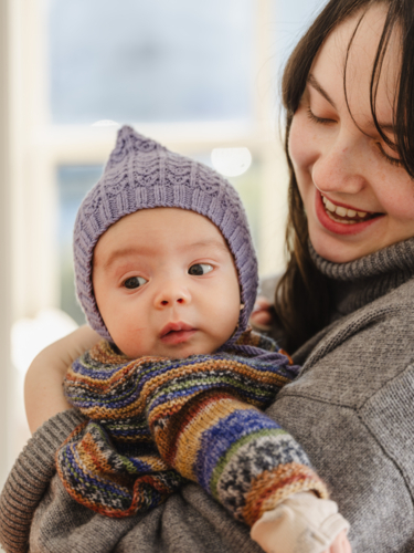 Young mother holding baby wearing beanie inside home - Australian Stock Image
