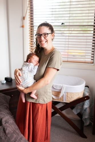 Young mother holding newborn baby in bedroom in home - Australian Stock Image