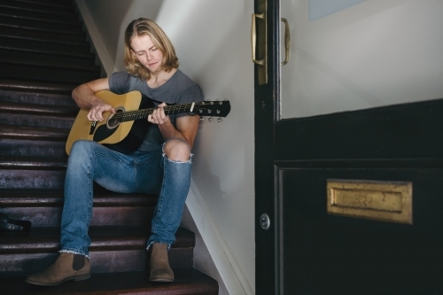 Young musician playing guitar on the stairs - Australian Stock Image
