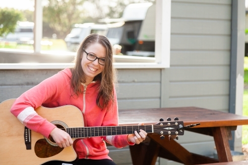 Young person playing guitar outside sitting on park bench - Australian Stock Image