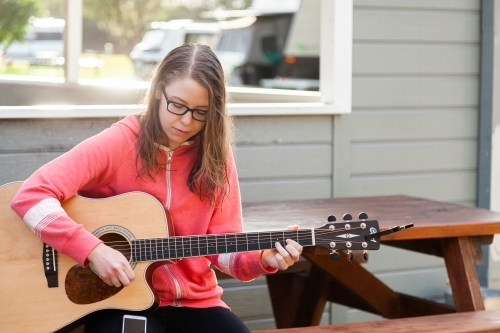 Young person playing guitar outside sitting on park bench - Australian Stock Image