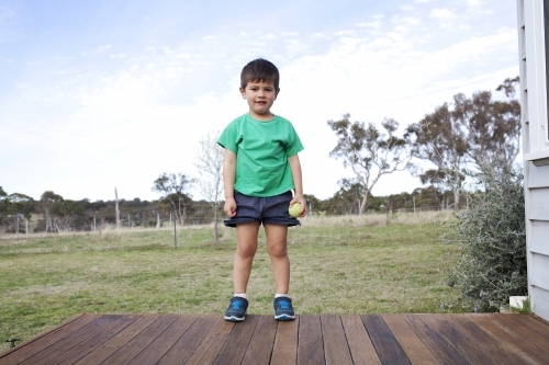 Young polynesian boy standing at the end of deck with countryside in the background - Australian Stock Image