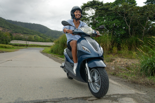 Young Polynesian man riding a scooter alone on a rural road in Far North Queensland - Australian Stock Image