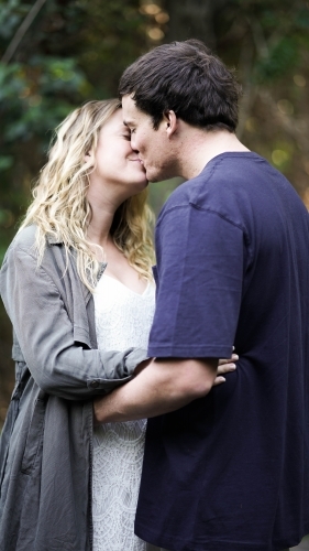 Young pregnant couple kissing, half length - Australian Stock Image