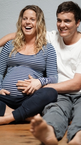 Young pregnant couple sitting against white wall