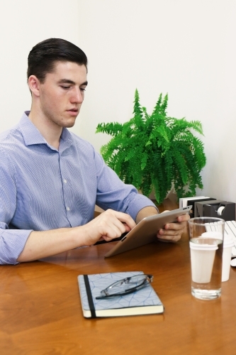Young professional man sitting at office desk using tablet