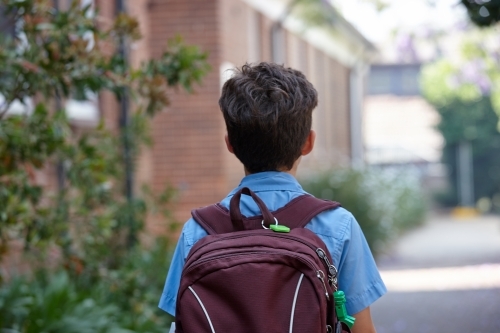 Young school boy walking away from camera, to class - Australian Stock Image