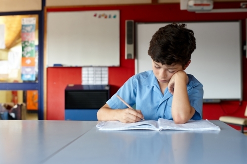 Young school boy working on homework in classroom - Australian Stock Image