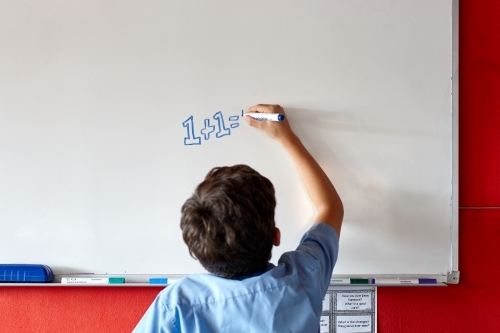 Young school boy writing on white board in class - Australian Stock Image