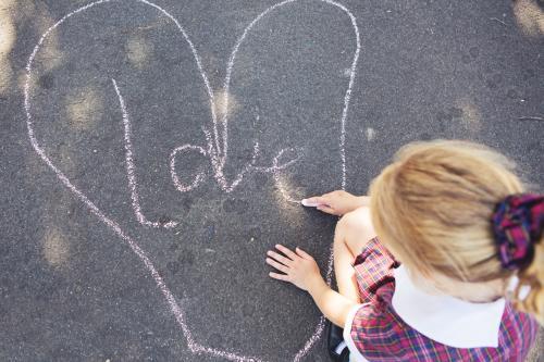 Young school girl drawing pictures on the road with chalk - Australian Stock Image