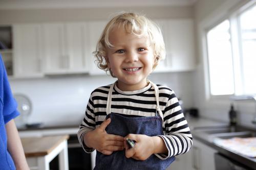 Young smiling boy wearing apron in kitchen - Australian Stock Image