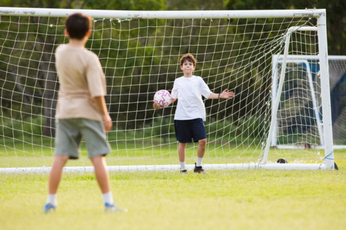 Young soccer player holding the soccer ball in front of soccer goal net during penalty kick - Australian Stock Image