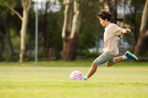 Young soccer player kicking soccer ball on grassy field - Australian Stock Image