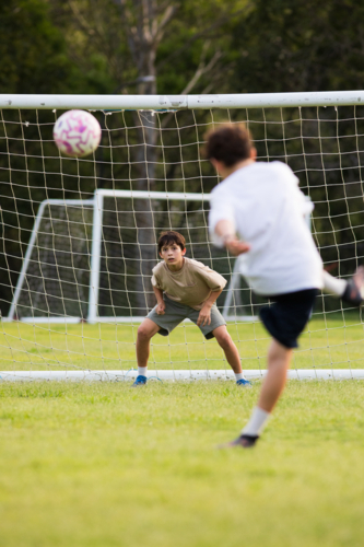 Young soccer player on defensive stance in front of soccer goal net during penalty kick - Australian Stock Image