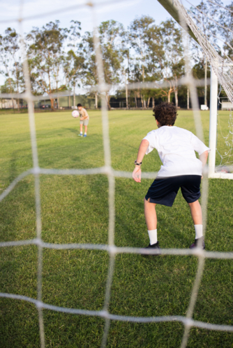 Young soccer player on defensive stance viewed through the soccer goal net during penalty kick - Australian Stock Image