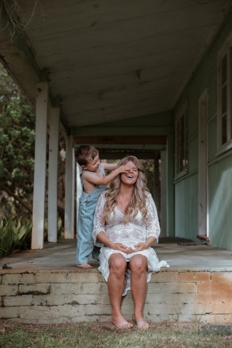 Young son covering his mother's eyes and playing with her on the front porch of home - Australian Stock Image