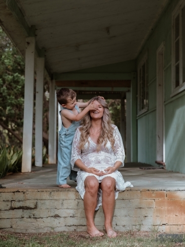 Young son covering his mother's eyes and playing with her on the front porch of home - Australian Stock Image