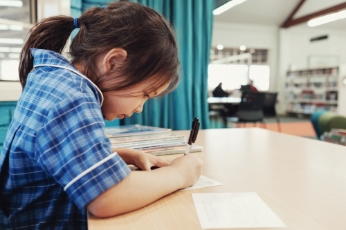 Young student girl writing in libary - Australian Stock Image