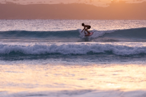 young surfer backlit surfing small waves at sunset - Australian Stock Image
