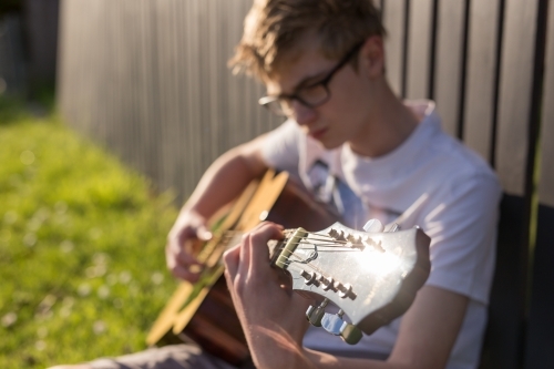 Young teen boy playing acoustic guitar by fence - Australian Stock Image