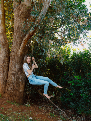 Young teenage girl hanging on a rope swing on the tree. - Australian Stock Image