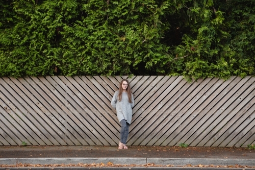 Young teenage girl in front of timber fence with green hedge