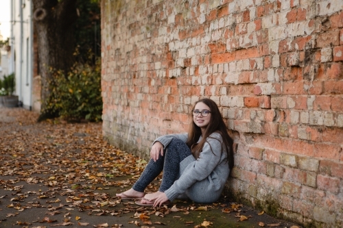 Young teenage girl leaning against red brick wall
