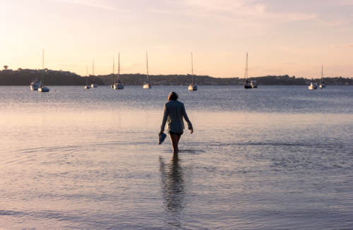 Young teenage girl standing in calm water in the late afternoon with boats in the background - Australian Stock Image