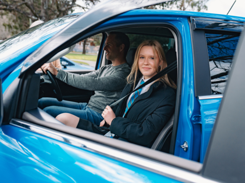 Young teenage student in school uniform sitting inside blue car fastening seatbelt - Australian Stock Image