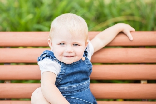 Young toddler girl sitting on bench seat - Australian Stock Image