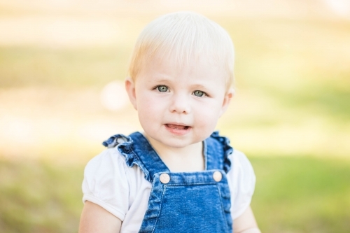 Young toddler girl with blonde hair sitting outdoors - Australian Stock Image