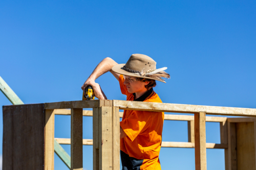 Young trainee trade apprentice building frame in bright sunlight against blue Australian sky - Australian Stock Image