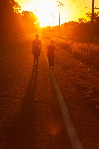 Young woman and young boy walking along the side of the road towards the sunset
