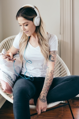Young woman at home with headphones connected to her smartphone - Australian Stock Image