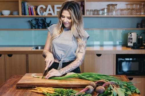 Young woman chopping vegetables preparing dinner at home - Australian Stock Image